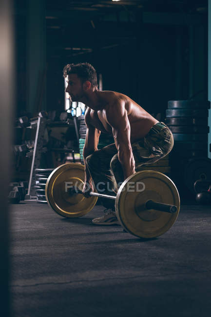 Uomo muscolare che si allena con il bilanciere nella sala fitness — Foto stock