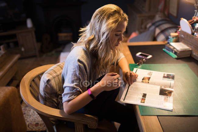 Jeune femme lisant un magazine assis sur une chaise à la maison — Photo de stock