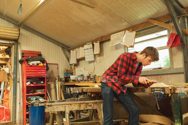 Joven carpintero masculino usando herramienta plana en taller - foto de stock