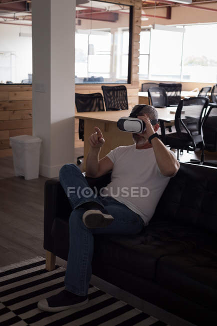 Чоловік керівник офісу відчуває гарнітуру віртуальної реальності на дивані в креативному офісі — стокове фото