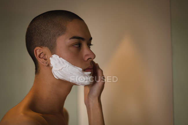 Молодий чоловік наносить крем для гоління на обличчя у ванній — стокове фото