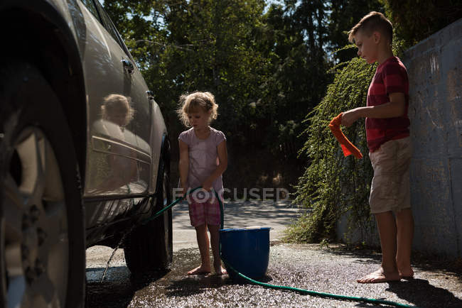Frères et sœurs lavant une voiture dans un garage extérieur par une journée ensoleillée — Photo de stock