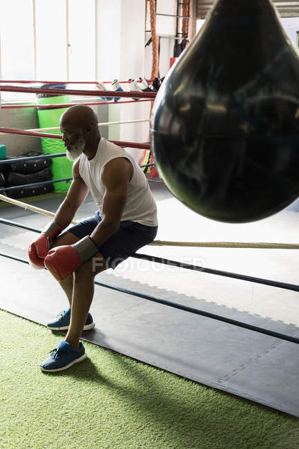 Homem idoso pensativo sentado no ringue de boxe no estúdio de fitness . — Fotografia de Stock