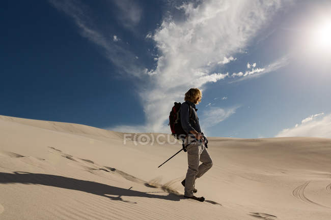 Caminhante masculino com poste de trekking andando na areia em um dia ensolarado — Fotografia de Stock