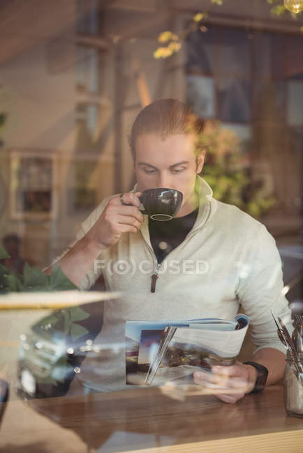 Homem tomando café enquanto lê revista no café — Fotografia de Stock