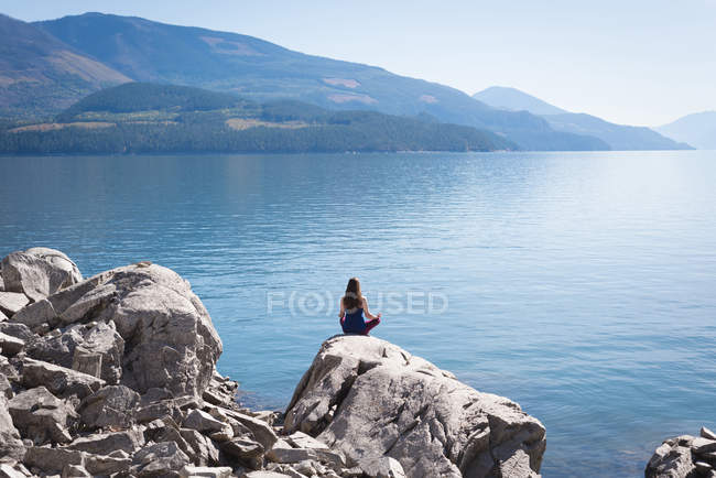 Femme pratiquant le yoga sur le rocher près de la mer — Photo de stock