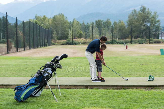 Pai ajudando seu filho a jogar golfe no campo — Fotografia de Stock
