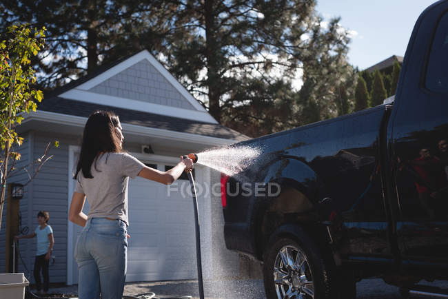 Vista posteriore della donna che lava la sua auto con un getto d'acqua ad alta pressione — Foto stock