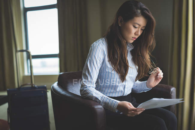 Documento di lettura da donna d'affari seduta sulla poltrona in camera d'albergo — Foto stock