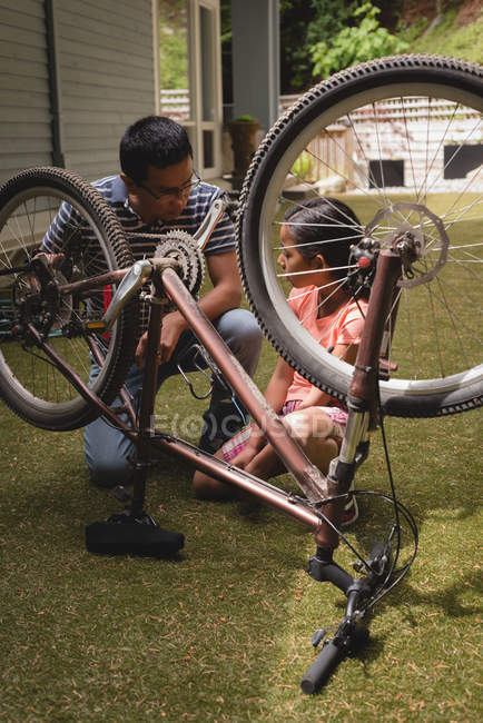 Père et fille interagissent les uns avec les autres tout en réparant le cycle dans le jardin — Photo de stock