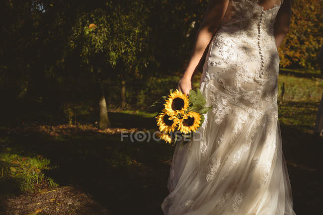 Vista trasera de la novia sosteniendo un ramo de girasol en el jardín - foto de stock