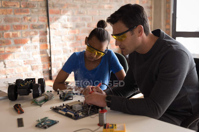 Father teaching daughter about soldering iron in office. — Stock Photo