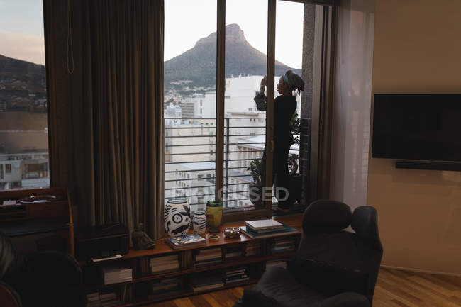 Interior de la habitación con estantes y silla y mujer tomando fotos con teléfono en el balcón . - foto de stock