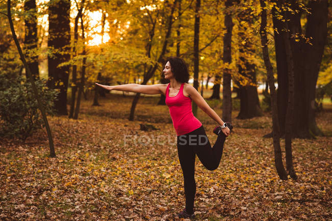 Femme effectuant un exercice d'étirement en forêt par une journée ensoleillée — Photo de stock