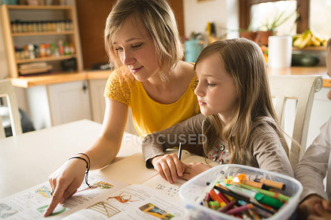 Mother helping daughter with homework in kitchen at home — Stock Photo