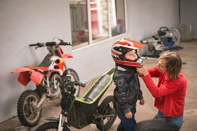 Madre preparando a su hijo para montar en bicicleta en el garaje - foto de stock