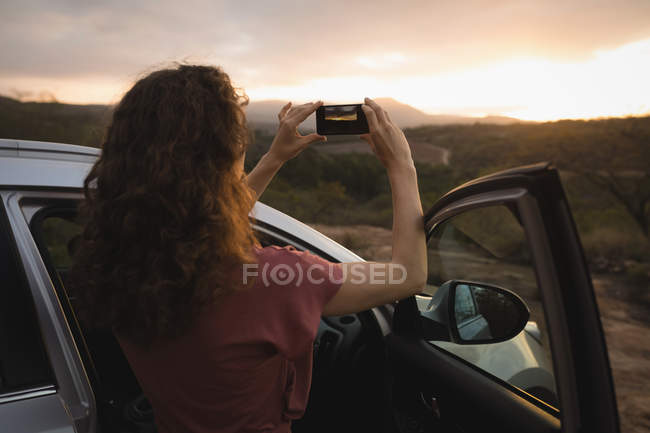 Жінка фотографує природу з мобільним телефоном на заході сонця — стокове фото