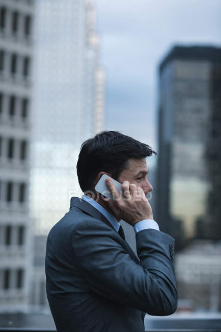 Seitenansicht eines Geschäftsmannes, der mit dem Handy gegen Wolkenkratzer spricht — Stockfoto