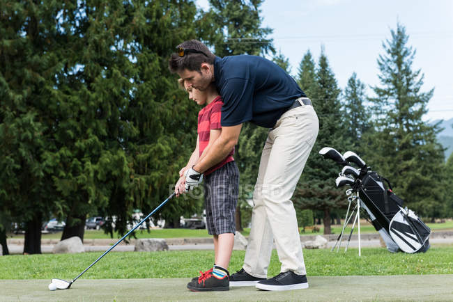 Father assisting his son to play golf in the course — Stock Photo