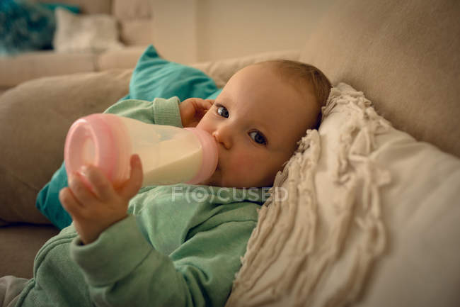 Menina bebê bebendo leite de mamadeira em casa — Fotografia de Stock