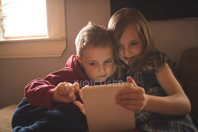 Happy sibling using tablet on sofa at home — Stock Photo