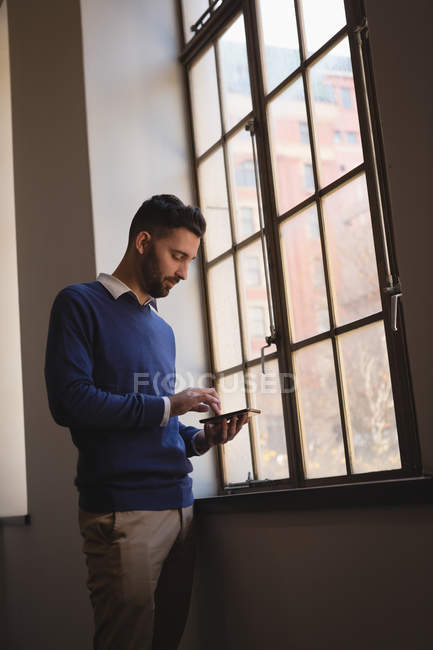 Jovem empresário usando telefone celular perto da janela no escritório . — Fotografia de Stock