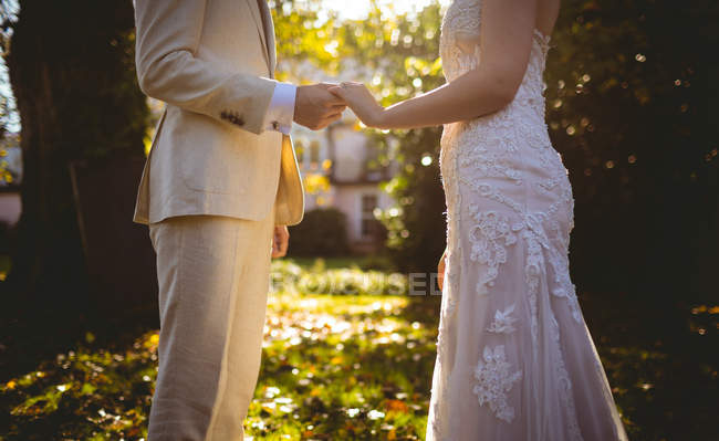 Средняя часть невесты и жениха, держащихся за руки в саду — стоковое фото