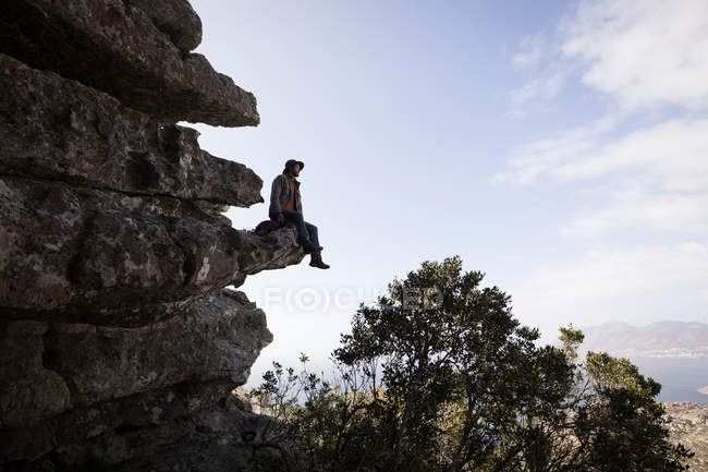 Caminante sentado en el acantilado de roca en un día soleado - foto de stock