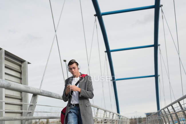 Young man walking on bridge while listening to music — Stock Photo