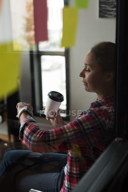 Жіночий керівник використовує смарт-годинник, маючи каву в офісі — стокове фото