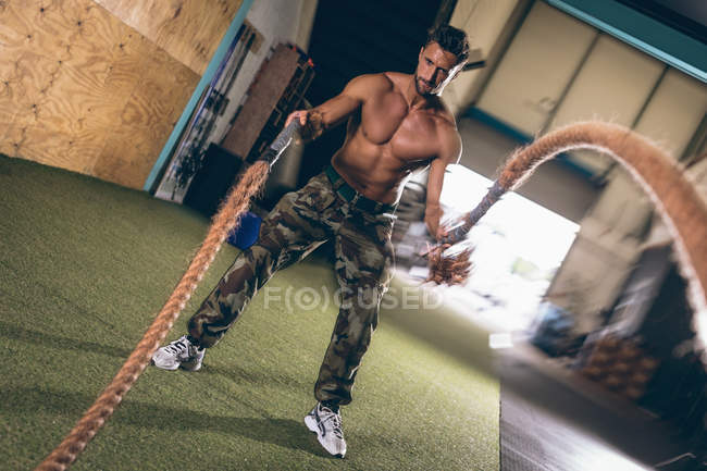 Hombre musculoso determinado haciendo ejercicio con cuerda en el gimnasio - foto de stock