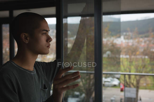 Nachdenklicher junger Mann schaut zu Hause durch Fenster — Stockfoto