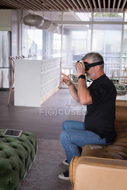 Ejecutiva de oficina masculina experimentando auriculares de realidad virtual en el sofá en la oficina creativa - foto de stock