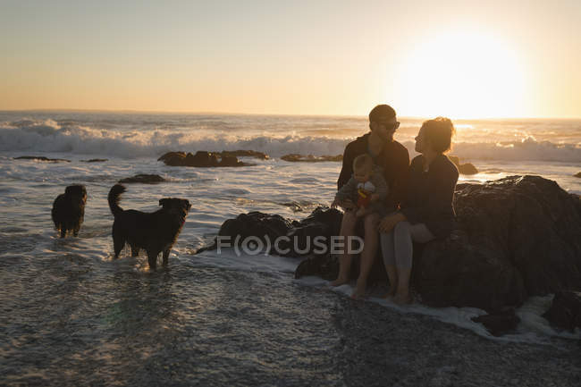 Família relaxante na rocha na praia durante o pôr do sol — Fotografia de Stock