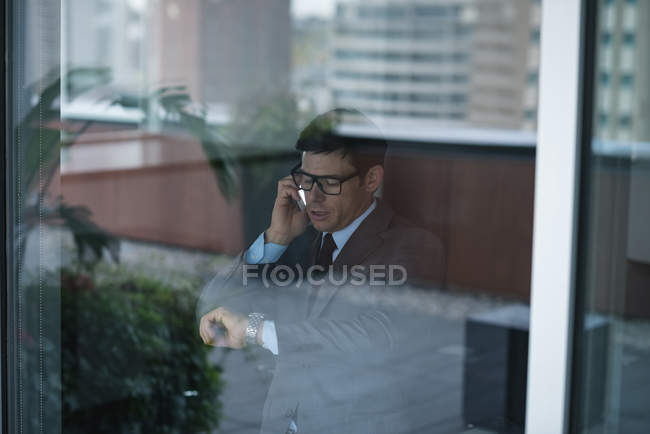 Бизнесмен разговаривает по телефону во время проверки времени в офисе — стоковое фото