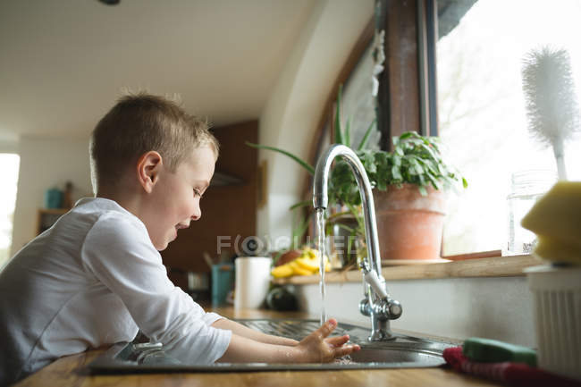 Мальчик моет руки на кухонной раковине дома — стоковое фото