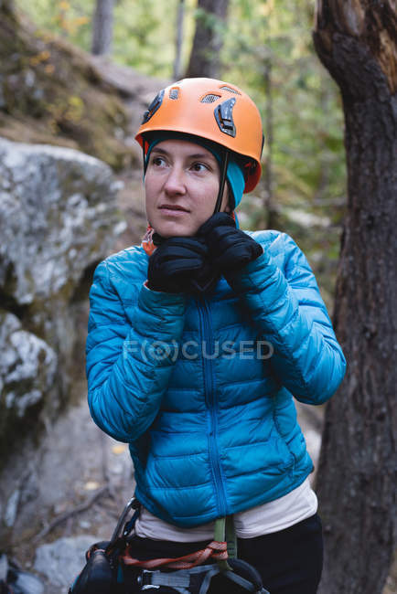 Escursionista femminile che regola il suo casco nella foresta — Foto stock