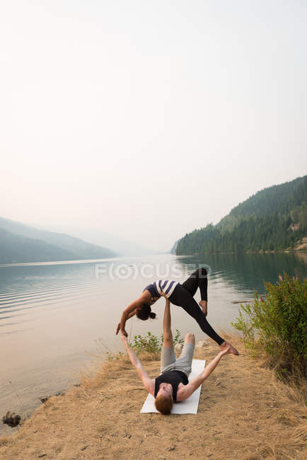 Pareja en forma practicando acro yoga en un exuberante terreno verde a la hora del amanecer - foto de stock