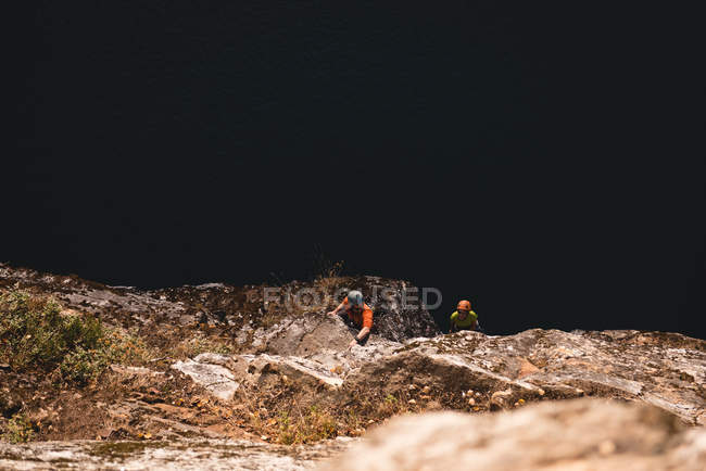 Determinada pareja de excursionistas escalando la montaña rocosa - foto de stock