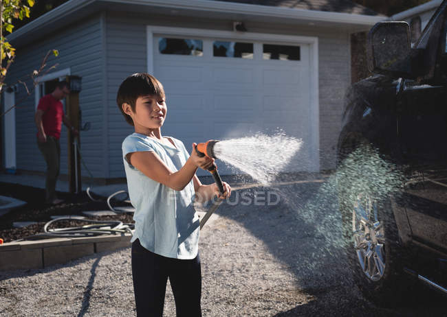 Junge wäscht Auto mit Hochdruck-Wasserstrahl außerhalb der Garage — Stockfoto