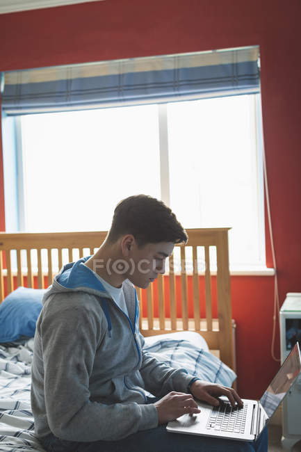 Young man working with laptop in bedroom interior. — Stock Photo