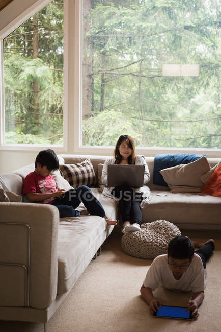 Mother using laptop while kids using digital tablet in living room at home — Stock Photo