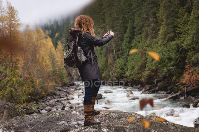 Femme photographiant le ruisseau dans la forêt d'automne — Photo de stock