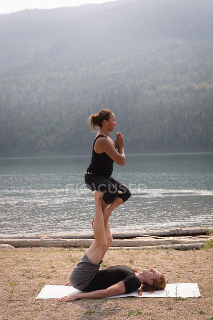 Vista lateral de mujeres deportistas practicando acro yoga cerca de la costa del mar - foto de stock