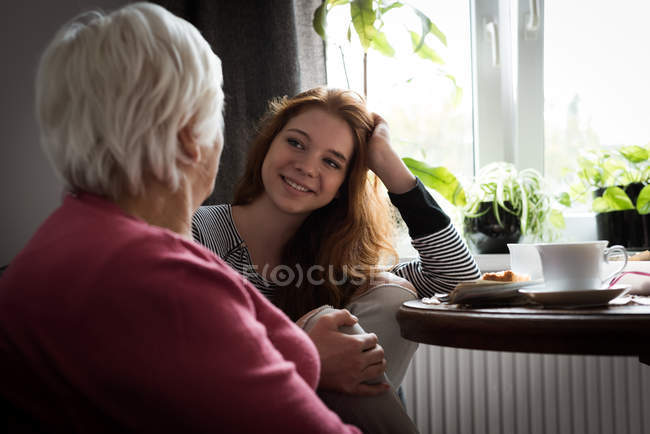 Усміхнена онука взаємодіє з бабусею у вітальні вдома — стокове фото