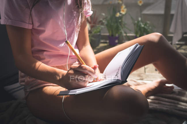 Крупним планом вигляд жінки, що пише в щоденнику, сидячи на підлозі біля дверей балкона . — стокове фото