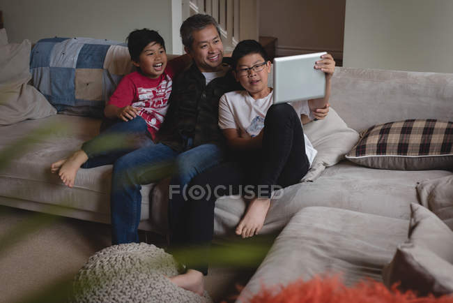 Padre e hijos que tienen videollamada en el ordenador portátil en la sala de estar en casa - foto de stock
