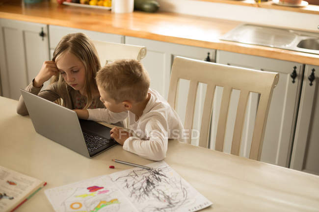 Enfants utilisant un ordinateur portable ensemble dans la cuisine à la maison — Photo de stock
