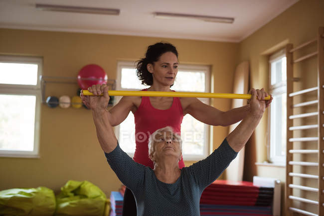 Женщина-терапевт помогает пожилой женщине с палкой для упражнений в доме престарелых — стоковое фото