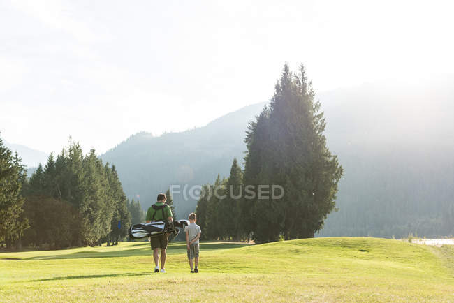 Vista trasera de padre e hijo caminando con club de golf en el campo - foto de stock